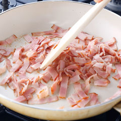 ベーコンから油が出てきたら少し混ぜてベーコンの表面に焼き目がつくように焼き、油を残してベーコンをとり出しておく。スパゲッティは塩を入れて沸騰させたお湯で、袋の表示時間より１分３０秒短く茹でる。茹で汁はとっておく。【コツ２】